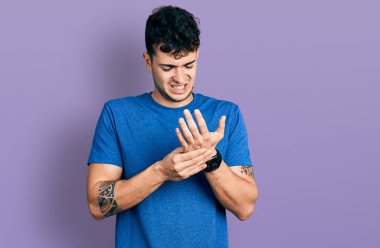 Ellerinde ve parmaklarında ağrı, eklem iltihabı olan gündelik tişört giyen İspanyol genç bir adam. 