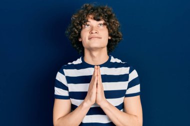 Yakışıklı, çizgili tişört giyen, elleri bağlı yalvaran ve dua eden, yüzünde umut ifadesi olan çok duygusal ve endişeli bir genç. Yalvarıyor. 