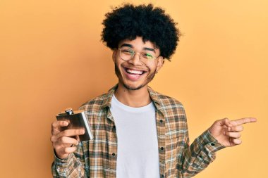 Afro saçlı, viski şişesinden alkol içen, eli ve parmağı kenarda mutlu bir şekilde gülümseyen Afro Amerikalı genç bir adam. 