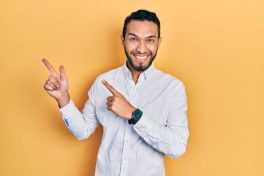 Sakallı, iş gömleği giyen, gülümseyen ve kameraya bakan iki eli ve parmakları yandan gösteren İspanyol bir adam.. 