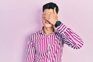 Latin asıllı genç bir adam, sıradan kıyafetler giyip gözlerini eliyle kapatıyor, ciddi ve üzgün görünüyor. Görme, saklama ve reddetme konsepti 