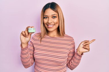 Güzel İspanyol kadın elinde kozmetik nemlendirici krem tutarken gülümsüyor. 