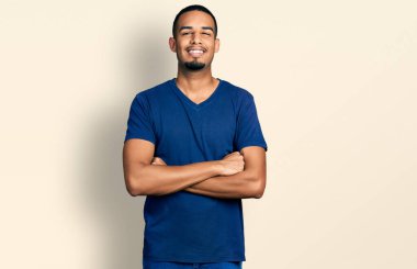 Kollarını kavuşturup gülümseyen, mutlu ve havalı gülümseyen genç Afro-Amerikalı bir adam. diş gösterme. 