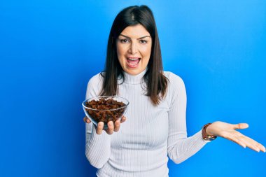 Genç İspanyol kadın elinde kuru üzüm kasesi tutarak başarıyı mutlu bir gülümsemeyle ve kazanan yüz ifadesiyle kutluyor. 