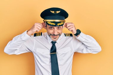 Yakışıklı, orta yaşlı, gri saçlı, uçak pilotu üniforması giyen, parmaklarıyla kulaklarını çeken, komik bir jest. deneme sorunu 