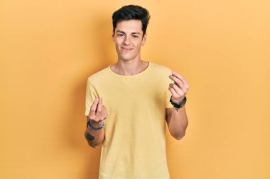 Latin asıllı genç bir adam günlük sarı tişört giyiyor. Elleriyle para hareketi yapıyor. Maaş ve milyonerlik işi istiyor. 