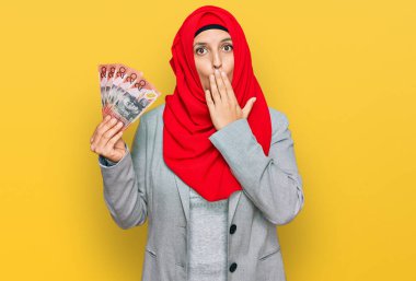 İslami başörtüsü takan güzel İspanyol bir kadın elinde Avustralya dolarları ile ağzı kaplayan banknotlar tutuyor, şaşırmış ve hata yapmaktan korkuyor. şaşırmış ifade 