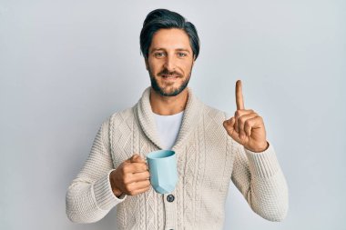 Genç İspanyol bir adam bir fincan kahve içiyor bir fikirle gülümsüyor ya da bir soru işareti yapıyor, bir numara: 