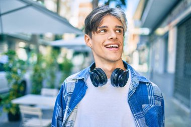 Genç İspanyol adam şehirde yürürken kulaklık takarak mutlu bir şekilde gülümsüyor..