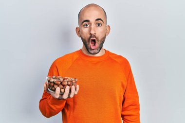 Genç kel adam elinde fındık tutuyor. Korkmuş ve ağzı açık kalmış, şaşırmış ve şaşırmış. 