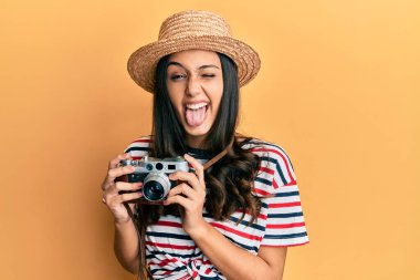 Yaz şapkası takan genç İspanyol kadın elinde antika bir kamera, dilini çıkarıp komik bir ifade takınıyor.. 