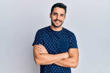 Gündelik kıyafetler giyen, kollarını kavuşturup kameraya gülümseyen genç İspanyol adam. pozitif kişi. 