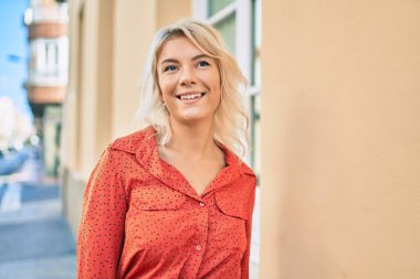 Genç sarışın kadın gülümseyerek şehirde mutlu mesut yürüyor..