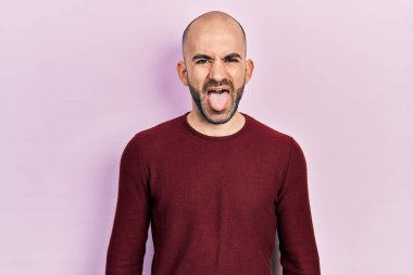 Sıradan kıyafetler giyen genç kel bir adam komik bir ifadeyle dilini dışarı çıkartıyor. duygu kavramı. 