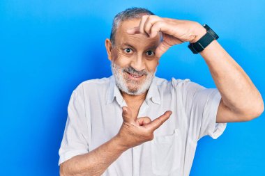 Sakallı, sıradan beyaz tişörtlü, yakışıklı, gülümseyen, elleri ve parmakları mutlu yüzlü bir adam. yaratıcılık ve fotoğrafçılık kavramı. 