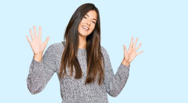 Kış süveteri giyen genç esmer kadın on numarayı gösterip işaret ederken kendinden emin ve mutlu bir şekilde gülümsüyor.. 