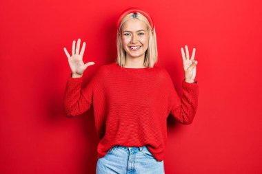 Güzel sarışın kadın gündelik kırmızı süveter giyer ve 8 numaralı parmaklarıyla işaret ederken kendinden emin ve mutlu gülümserdi.. 