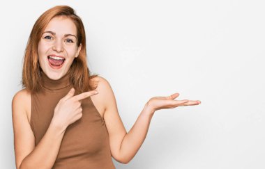 Gündelik giysiler giyen genç beyaz kadın kameraya hayret ediyor ve gülümsüyor.. 