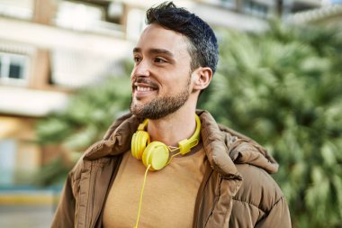 Şehirde kulaklık takarak mutlu gülümseyen genç İspanyol adam..