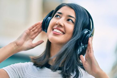 Genç İspanyol kadın gülümseyerek şehirde kulaklık takarak müzik dinliyor..