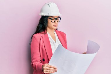 Ortadoğulu güzel bir kadın, güvenlik kaskı takan ve yüzünde ciddi bir ifade olan kağıt planlara bakıyor. Basit ve doğal bir şekilde kameraya bakıyorsun.. 