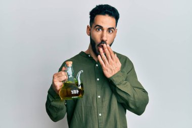 Elinde zeytinyağı olan genç İspanyol bir adam ağzını eliyle kapatıyor, şaşırmış ve hata yapmaktan korkuyor. şaşırmış ifade 