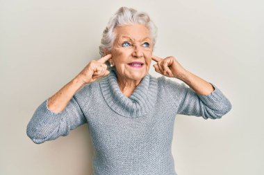 Yaşlı gri saçlı kadın parmaklarıyla kulaklarını kapatıyor. Gülümsüyor, yan tarafa bakıyor ve düşünüyor.. 