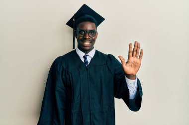 Mezuniyet şapkası ve tören cübbesi takan yakışıklı siyah adam beş numarayı gösterip işaret ederken kendinden emin ve mutlu gülümsüyor.. 