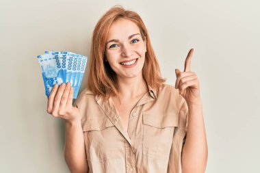 Elinde 10000 Şili pezosu olan beyaz bir kadın bir fikir veya soruyla gülümsüyor ve mutlu bir yüzle işaret ediyor. 