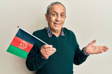 Beyaz saçlı yakışıklı son sınıf öğrencisi. Afgan bayrağı taşıyor. Başarı kutlamalarını mutlu bir gülümsemeyle ve kazanan ifadeyle el kaldırarak yapıyor. 