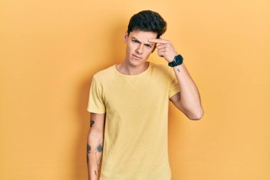 Gündelik sarı tişört giyen genç İspanyol adam alnındaki sivilceden mutsuz olduğunu gösteriyor. Siyah noktalı çirkin bir enfeksiyon. sivilce ve deri problemi 