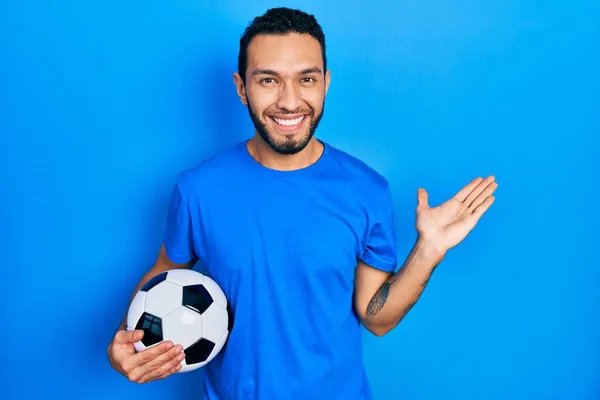 Латиноамериканець Бородою Тримає Футбольний Посміхаючись Радісно Презентуючи Вказуючи Пальмою Руки — стокове фото