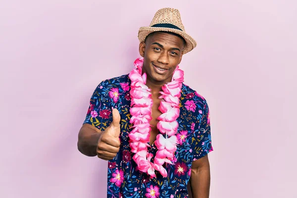 夏のシャツを着た若い黒人男性とハワイのレイは幸せと肯定的な笑みを浮かべて 親指アップ素晴らしいと承認サインを行う — ストック写真