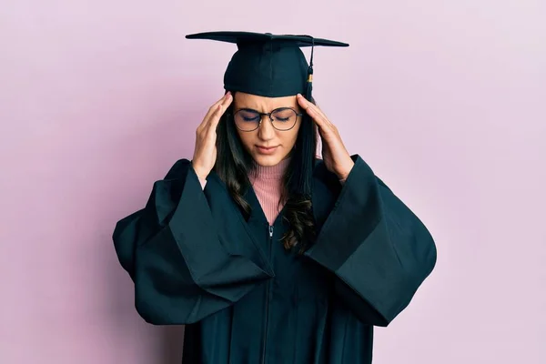ストレスが原因で頭の中で痛みのために頭の上に手で卒業キャップと式のローブを身に着けている若いヒスパニック系の女性 片頭痛 — ストック写真