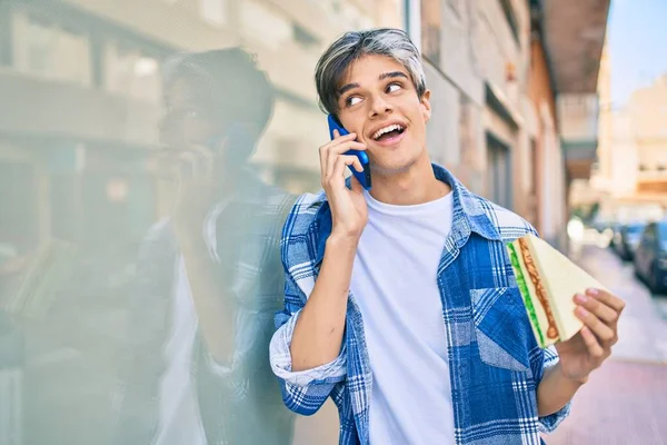 Joven Hombre Hispano Sonriendo Feliz Hablando Smartphone Comiendo Sándwich Ciudad —  Fotos de Stock