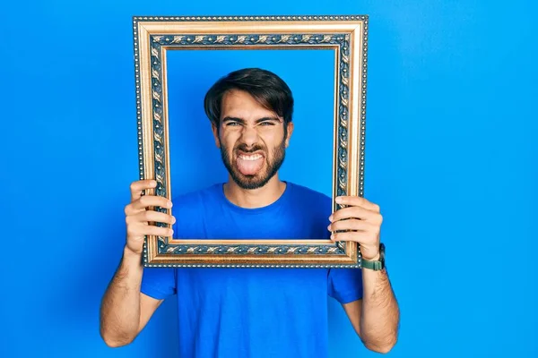 Mladý Hispánec Drží Prázdný Rám Vyčnívat Jazyk Šťastný Legračním Výrazem — Stock fotografie