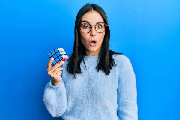 stock image Young brunette woman playing colorful puzzle cube intelligence game scared and amazed with open mouth for surprise, disbelief face 