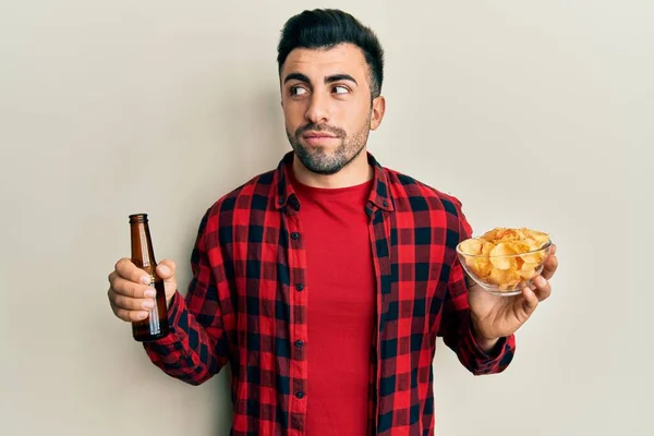 Joven Hispano Bebiendo Una Botella Cerveza Comiendo Papas Fritas Sonriendo — Foto de Stock