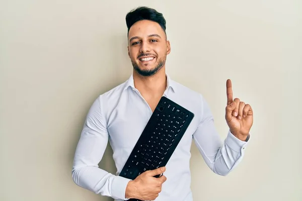 Młody Arabski Mężczyzna Trzymający Klawiaturę Komputerową Uśmiechnięty Pomysłem Lub Pytaniem — Zdjęcie stockowe