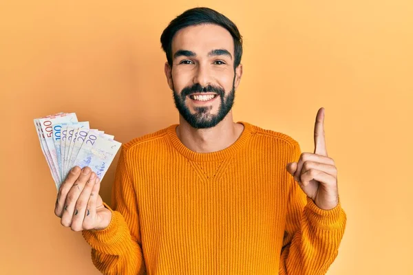 若いヒスパニック系の男は幸せな顔をしたアイデアや質問指差し指で笑顔スウェーデンクローナ紙幣を保持 ナンバーワン — ストック写真