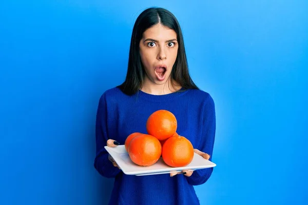 Mujer Hispana Joven Sosteniendo Plato Con Naranjas Frescas Asustada Conmocionada —  Fotos de Stock