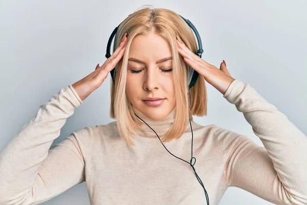 痛みや片頭痛のため 必死に頭痛やストレスに苦しんでヘッドフォンを使用して音楽を聞いて若いブロンドの女性 手を頭に — ストック写真