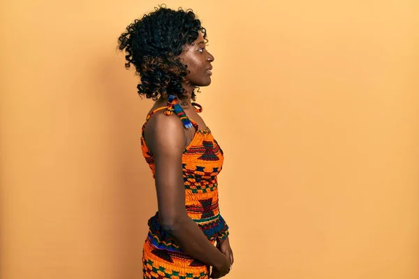 横に見える伝統的なアフリカの服を着て若いアフリカ系アメリカ人女性 自信を持って笑顔で自然な顔でプロファイルポーズをリラックス — ストック写真