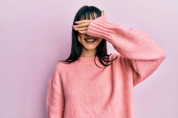 Young brunette woman with bangs wearing casual winter sweater smiling and laughing with hand on face covering eyes for surprise. blind concept.