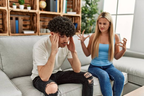 Молодая пара, сидящая на диване и обсуждающая дома.