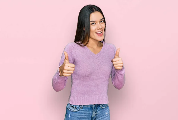 若いヒスパニック系の女の子の手で積極的なジェスチャーを行うカジュアルな服の成功のサインを着て 親指を笑顔と幸せ 陽気な表情と勝者のジェスチャー — ストック写真