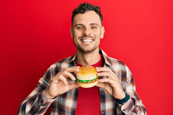 Fiatal Spanyol Férfi Eszik Egy Ízletes Klasszikus Hamburgert Mosolyogva Boldog — Stock Fotó