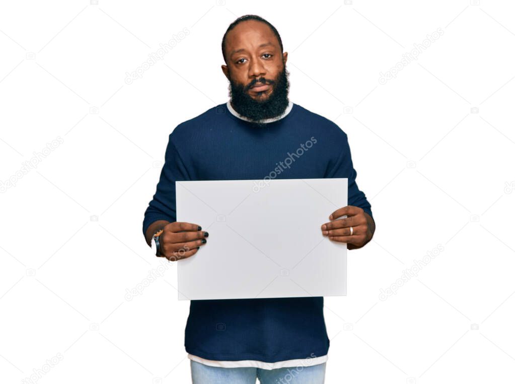 Young african american man holding blank empty banner thinking attitude and sober expression looking self confident 
