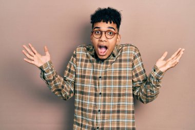 Gündelik kıyafetler ve gözlük takan genç Afro-Amerikan adam zaferi mutlu bir gülümsemeyle ve kazanan yüz ifadesiyle kutluyor. 