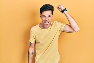 Genç, İspanyol asıllı, günlük sarı tişört giyen kızgın ve kızgın yumruğunu kaldırırken öfkeyle bağıran adam. öfke ve agresif konsept. 